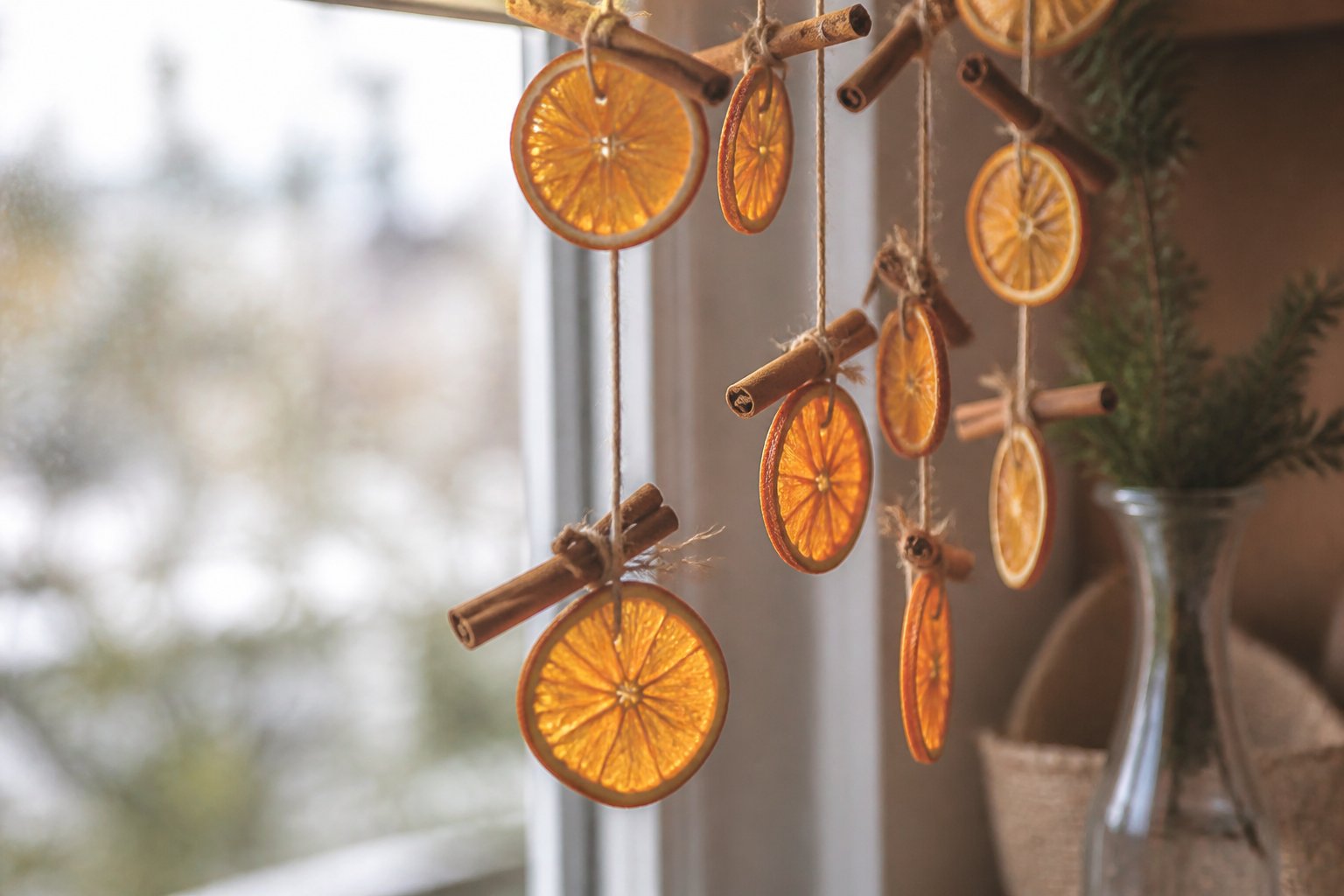 Tranches d’orange séchées enfilées sur une ficelle avec des bâtons de cannelle, suspendues devant une fenêtre